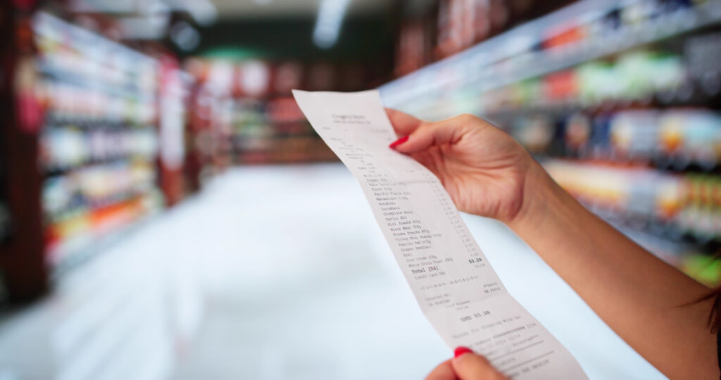 A person shopping in a grocery store and looking at her receipt, which will be easier to pay with the Canada Groceries and Essentials Benefit